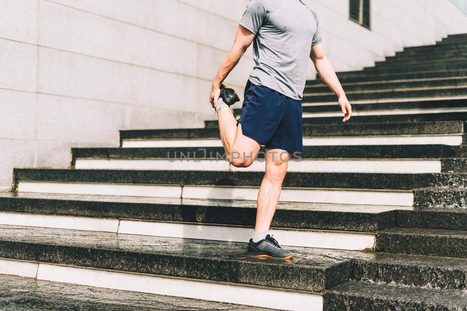 Young athlete man runner running up and down on city stairs in summer on morning run, background urban city street. Sports training. Fitness cardio workout in fresh air, walk outside.