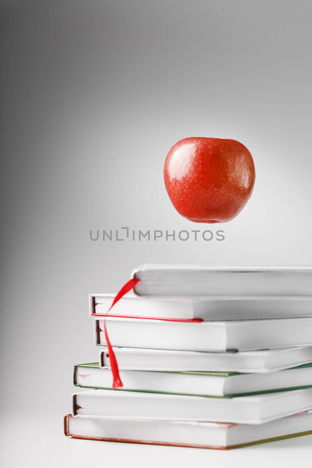 A red Apple hovers over a stack of books on a light background. by AlexGrec