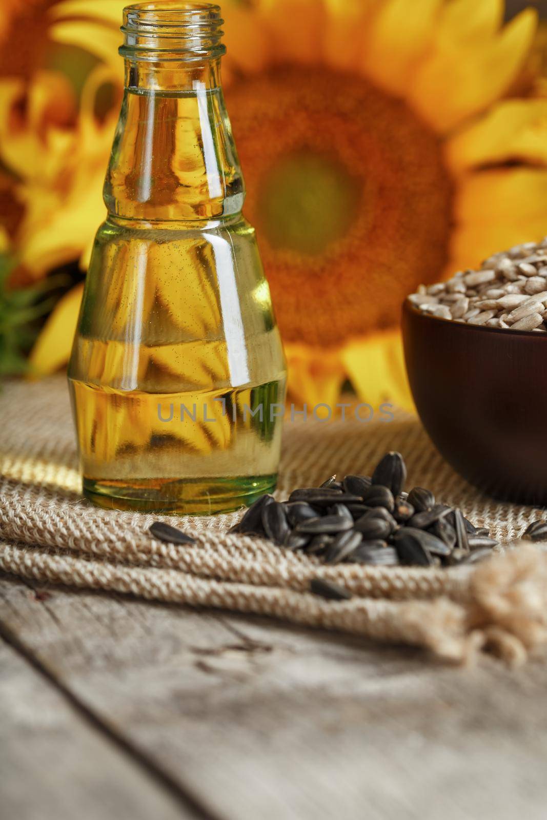Sunflower oil in a bottle with sunflower seeds and flowers on a wooden background. Composition in the village style. The concept of a bio-organic product. The vertical composition.