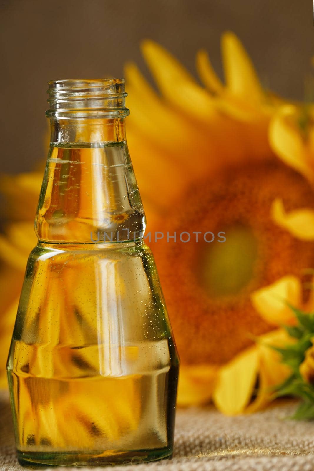 Sunflower oil in a glass bottle and flowers on a wooden background, close-up. Composition in the village style. The concept of a bio-organic product. The vertical composition.