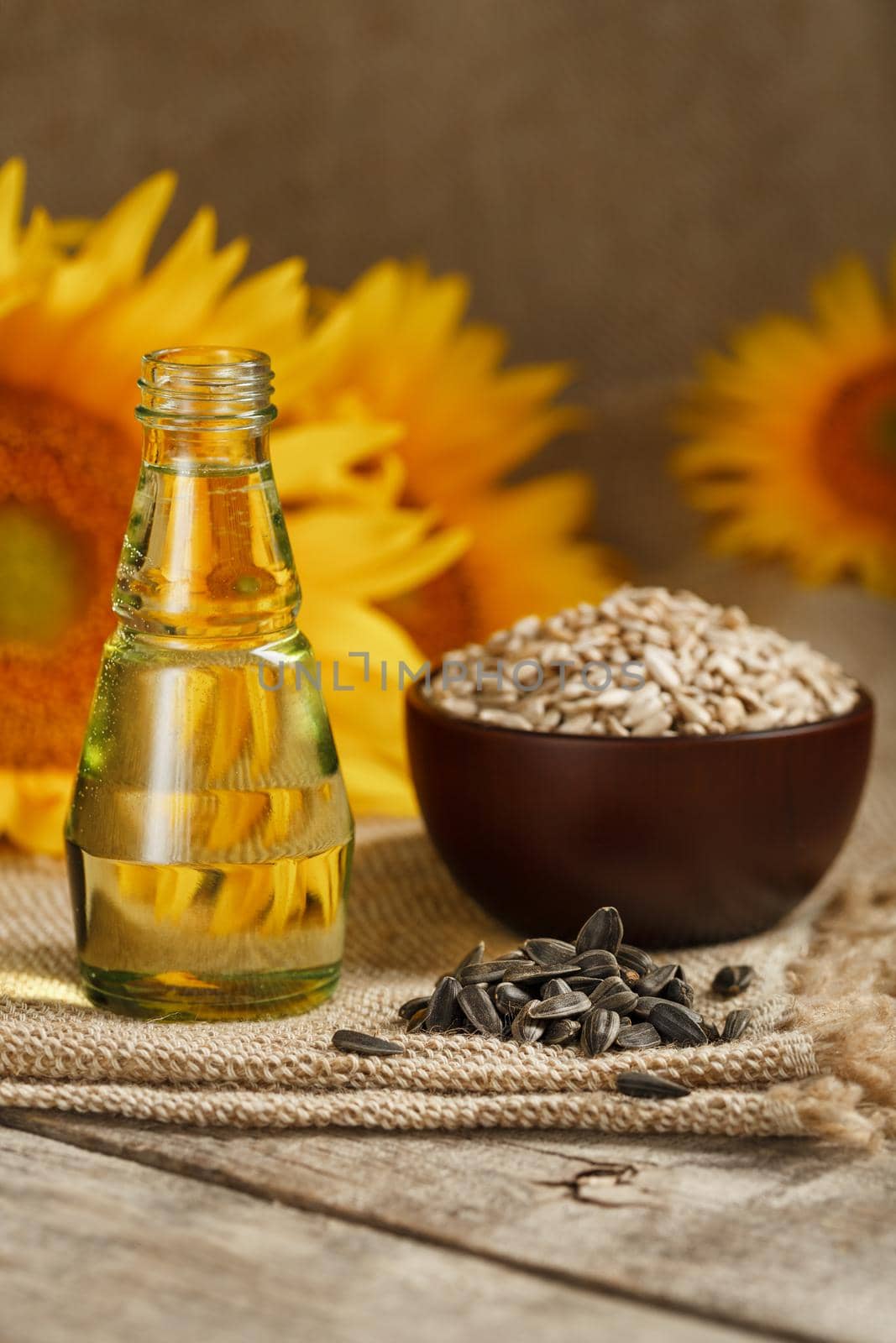 Sunflower oil in a glass bottle with seeds in a Cup and flowers on a wooden table. Composition in the village style. The vertical composition.