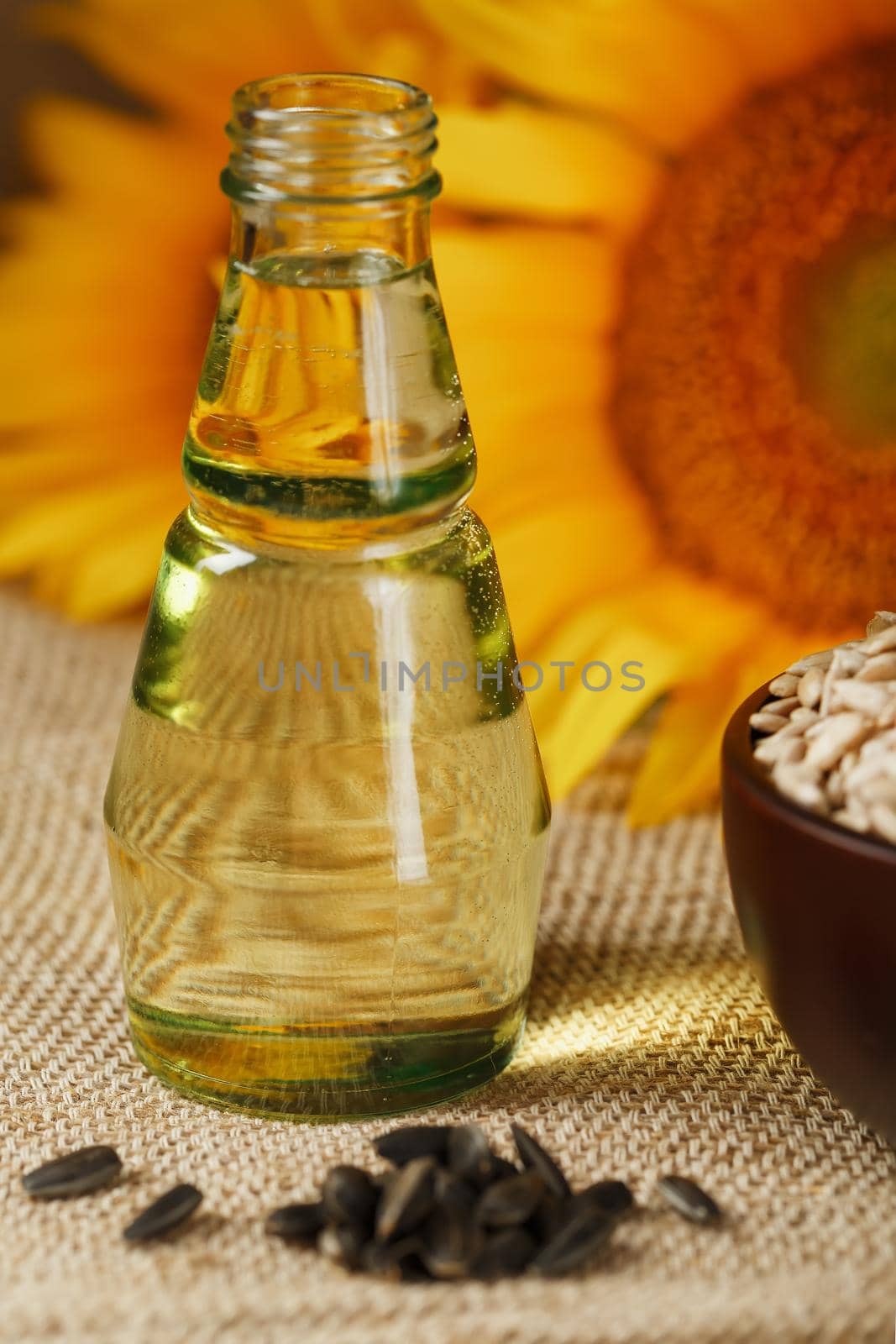 Sunflower oil in a glass bottle and flowers on a wooden background, close-up. Composition in the village style. The concept of a bio-organic product. The vertical composition.