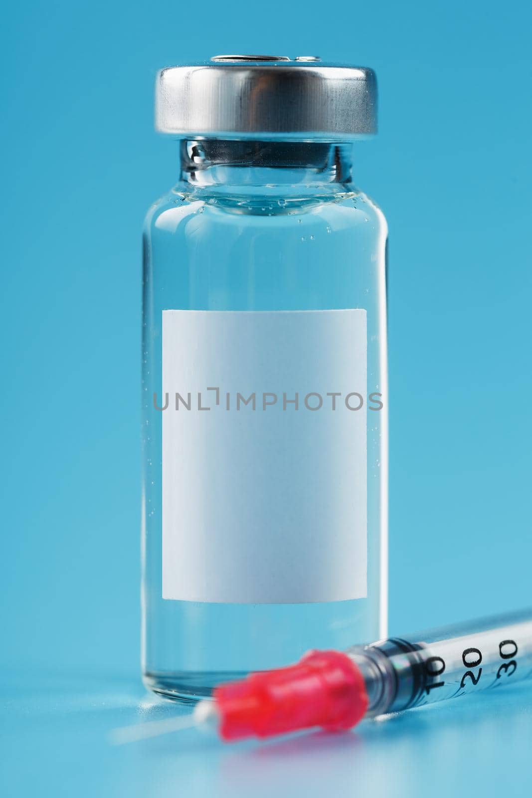 Ampoule with a vaccine and a syringe for viruses and diseases on a blue background. Free space on the ampoule for text. Isolate, vertical frame