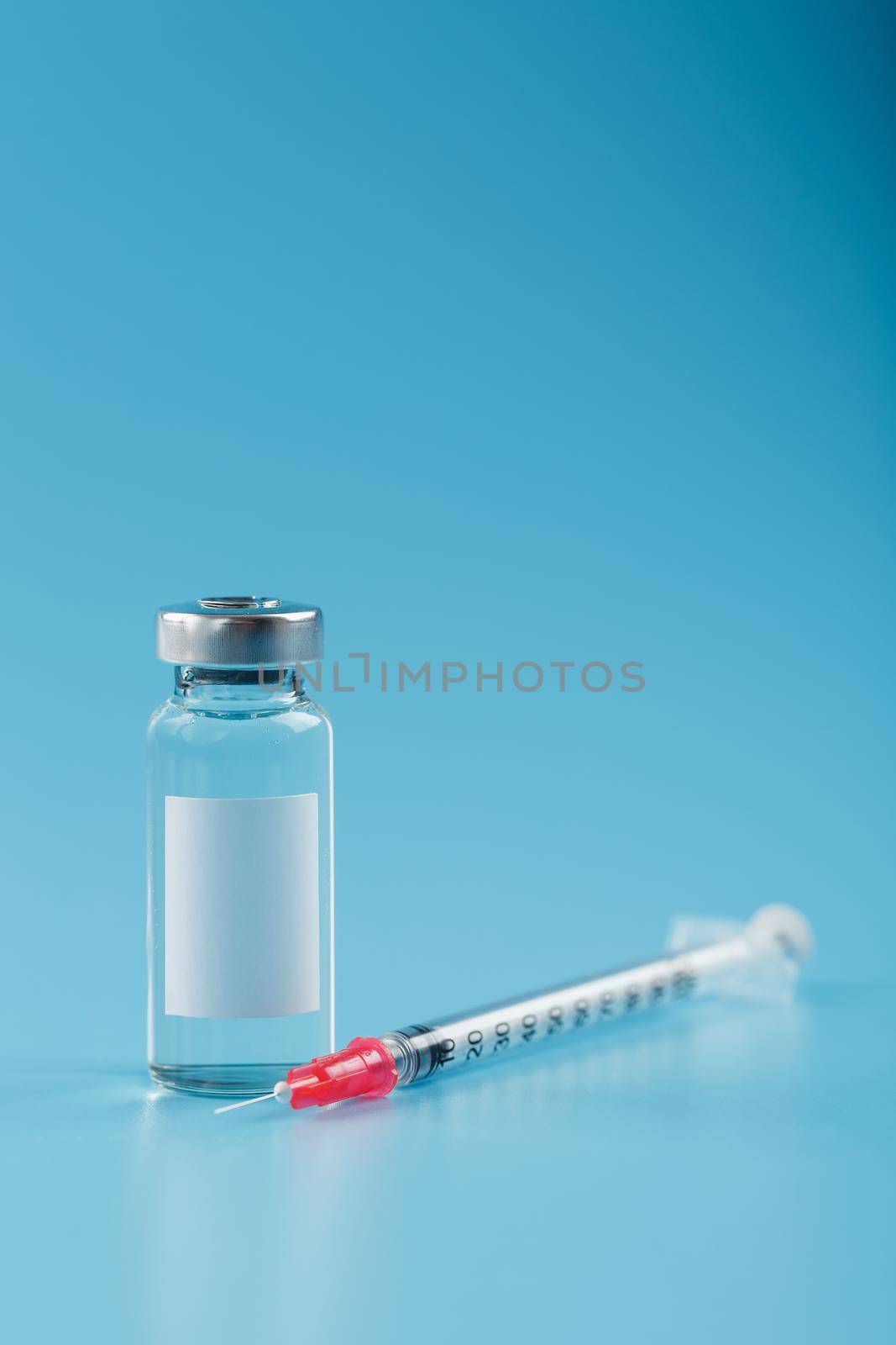 Syringe and ampoule with a vaccine against viruses and diseases on a blue background. Free space on the ampoule label for text, vertical frame
