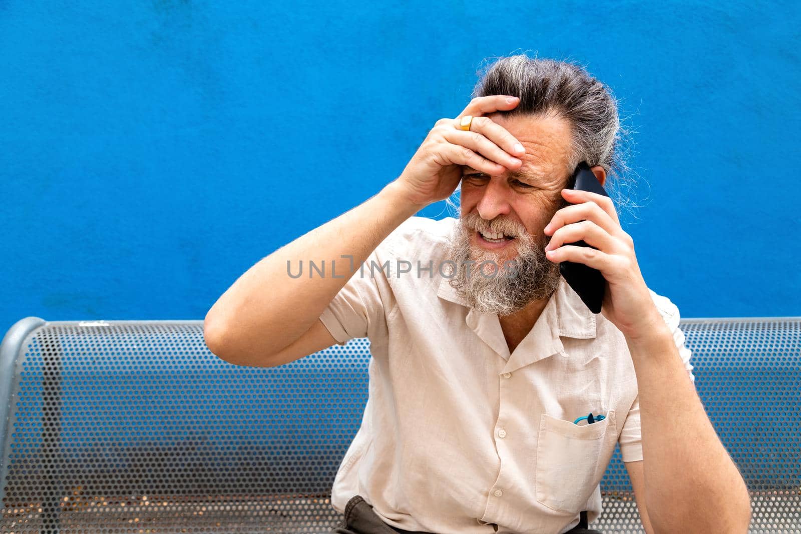 Worried mature caucasian man talking with mobile phone with hand on forehead. Copy space. by Hoverstock
