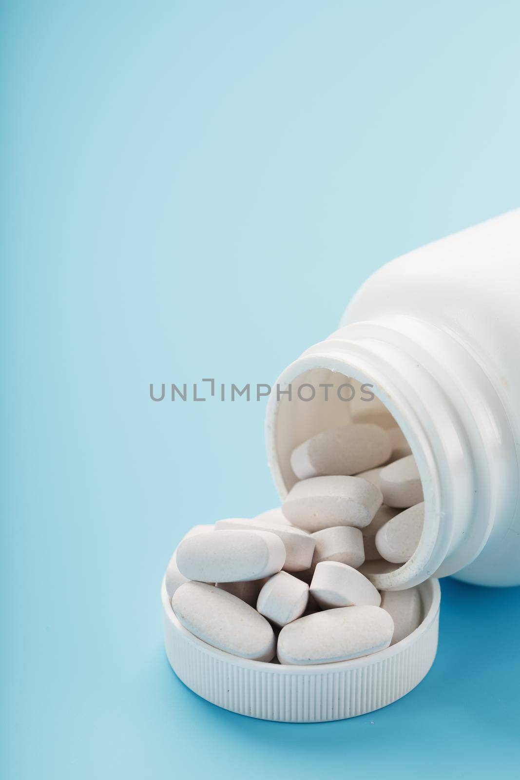 Vitamins and minerals in white capsules fell out of a white jar on a blue background. The concept of immune protection, antiviral prevention. Food additives. Free space