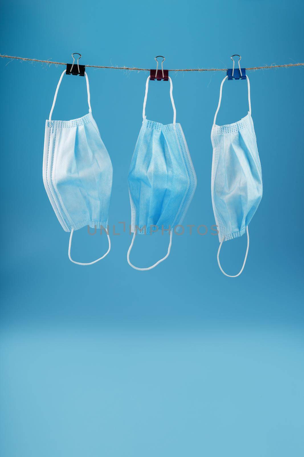 Three surgical masks hang on a clothesline against a blue background. Free space