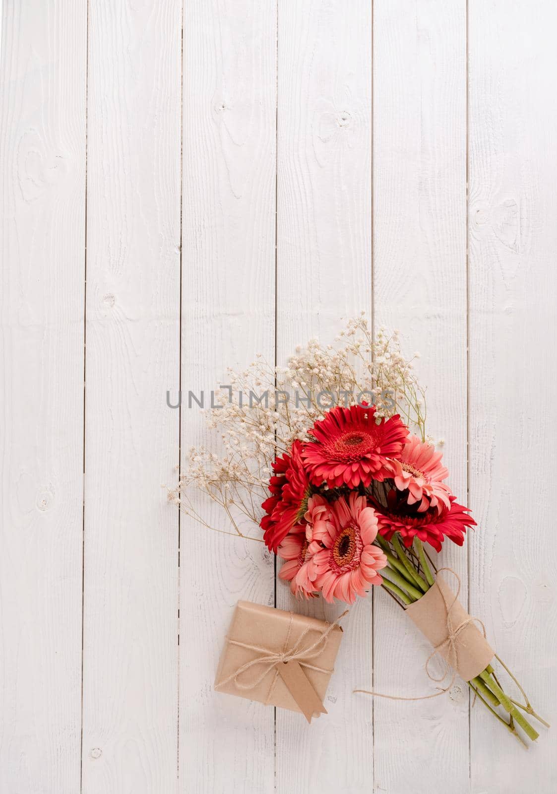 Happy birthday. Red gerbera daisy flowers and craft gift box with label tag on white wooden table, flat lay
