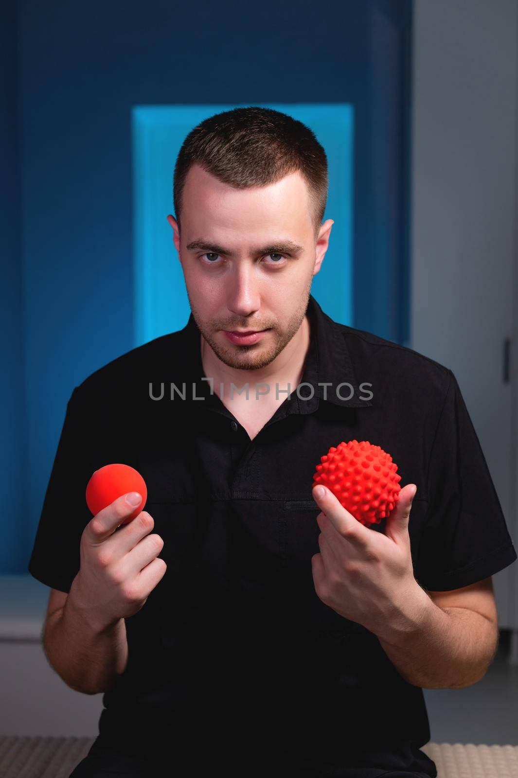 Attractive Caucasian young male masseur holding two massage balls in his hands and looking into the camera. Choice of instruments for self-massage by yanik88