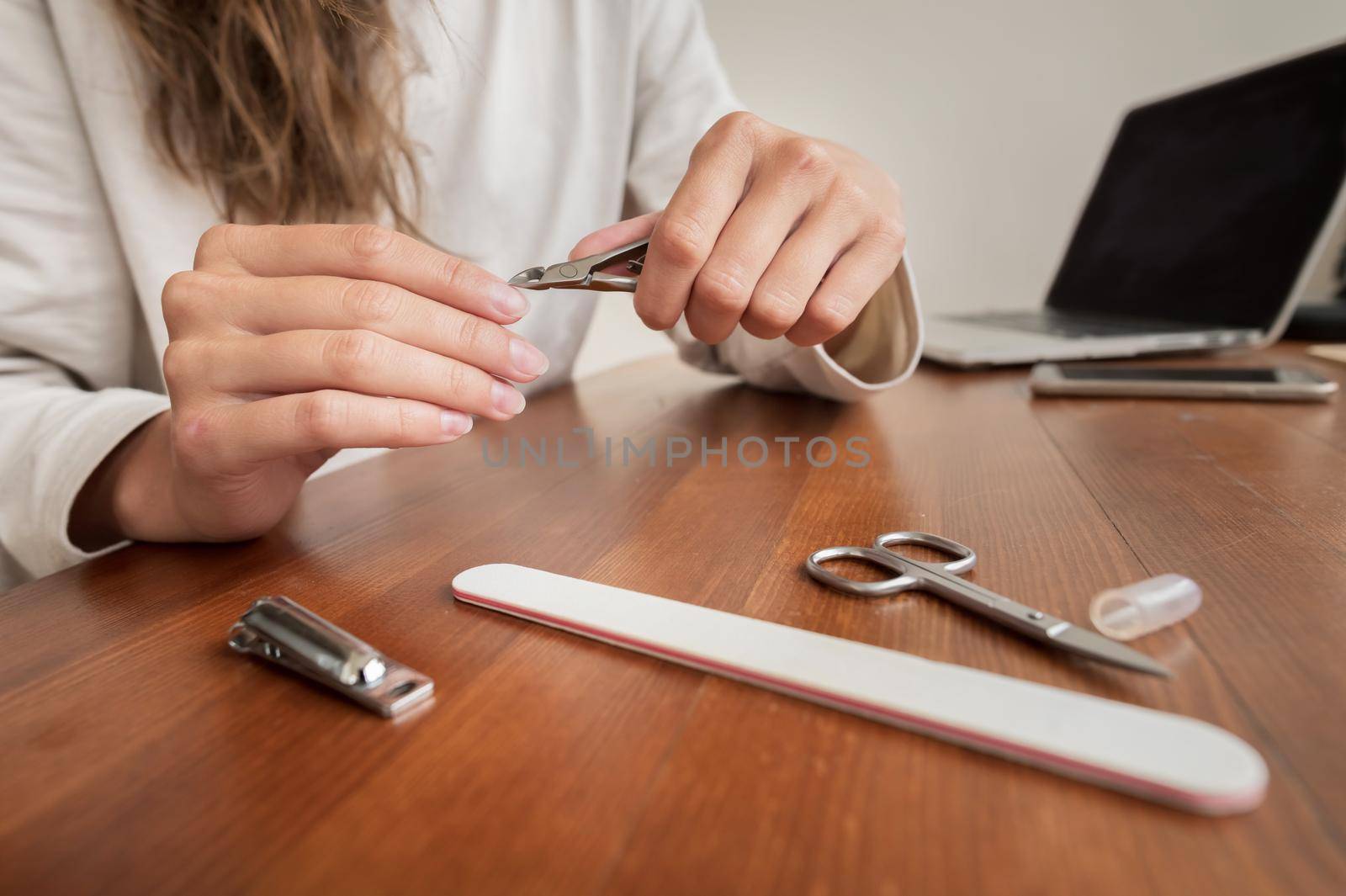 Young caucasian beautiful woman is sitting on a chair in the kitchen at home, busy with her beauty routine, tidies up and beauty her nails on her hands by yanik88