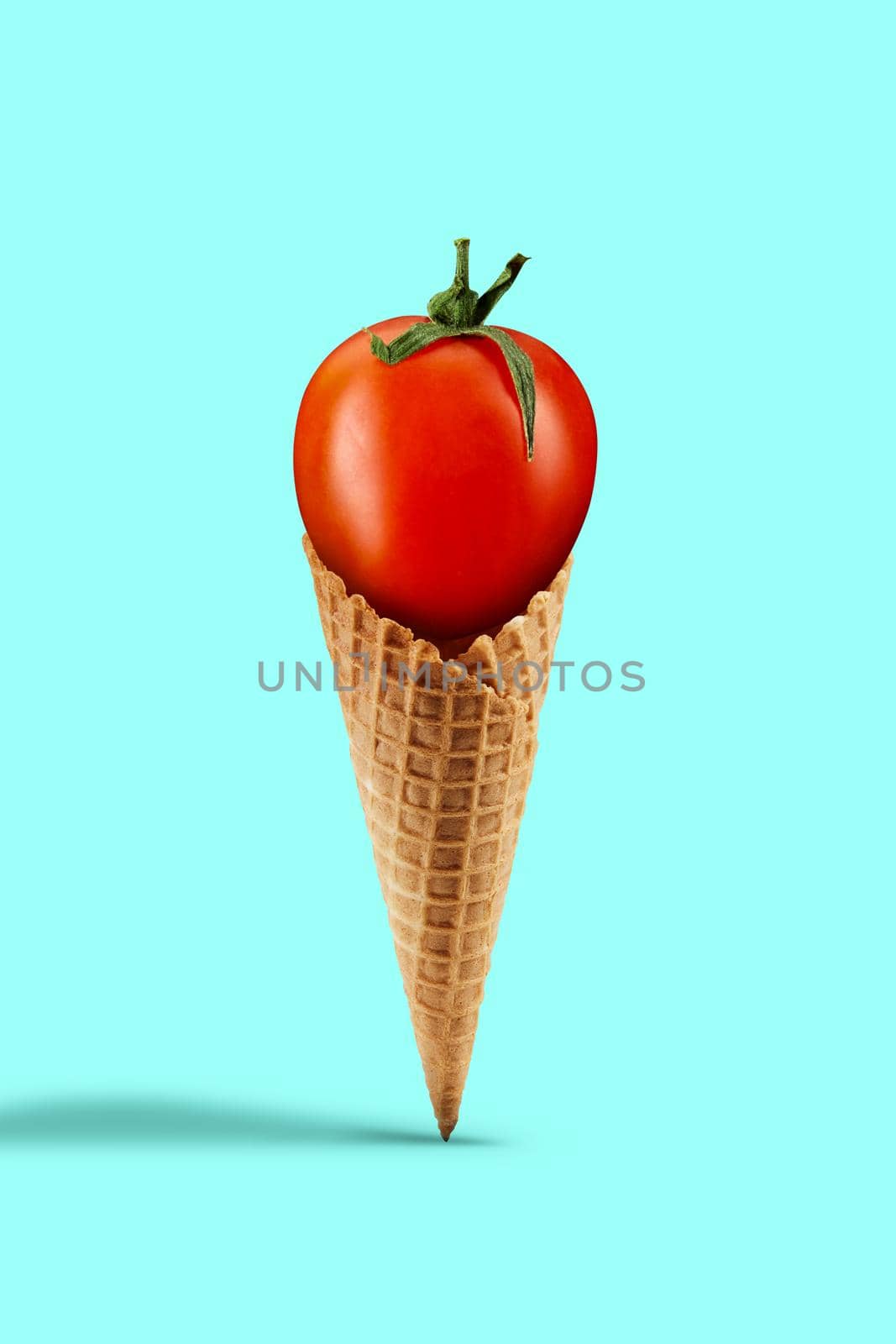 Ripe red tomato in a waffle cone over turquoise background. Concept of healthy nutrition, food and seasonal vegetables harvest. Close up, copy space