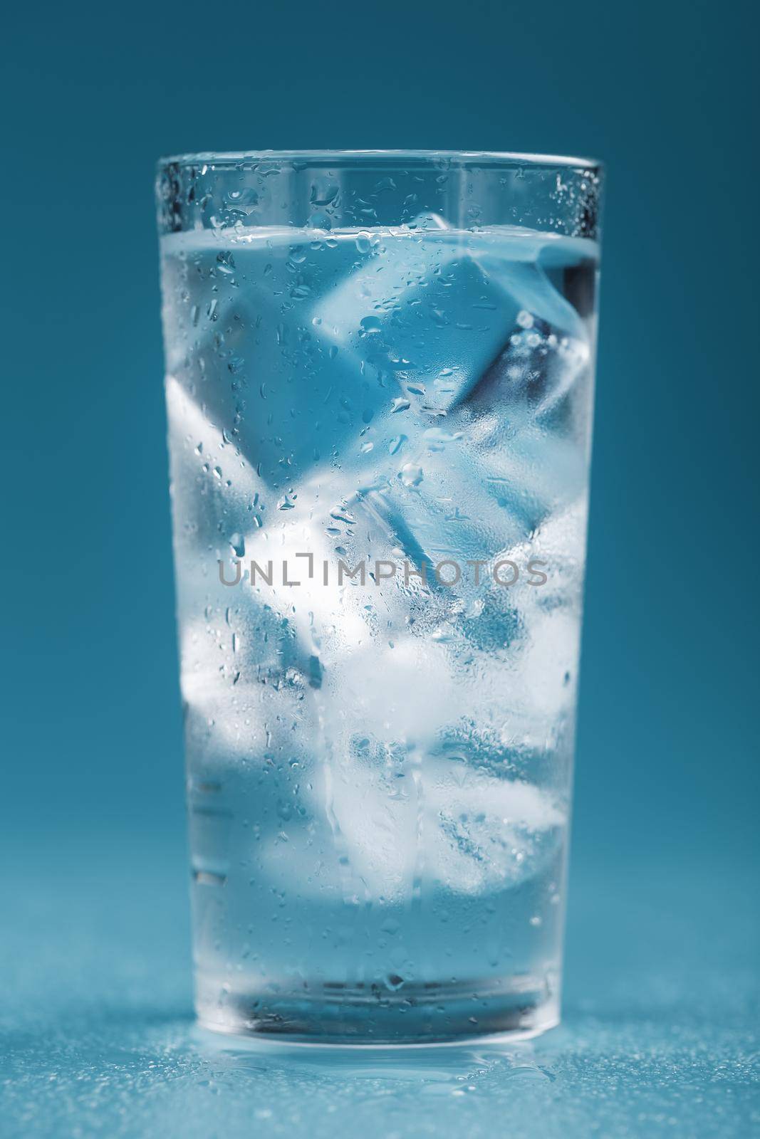Ice cubes in a glass with crystal clear water on a blue background. Refreshing and healthy water on hot days