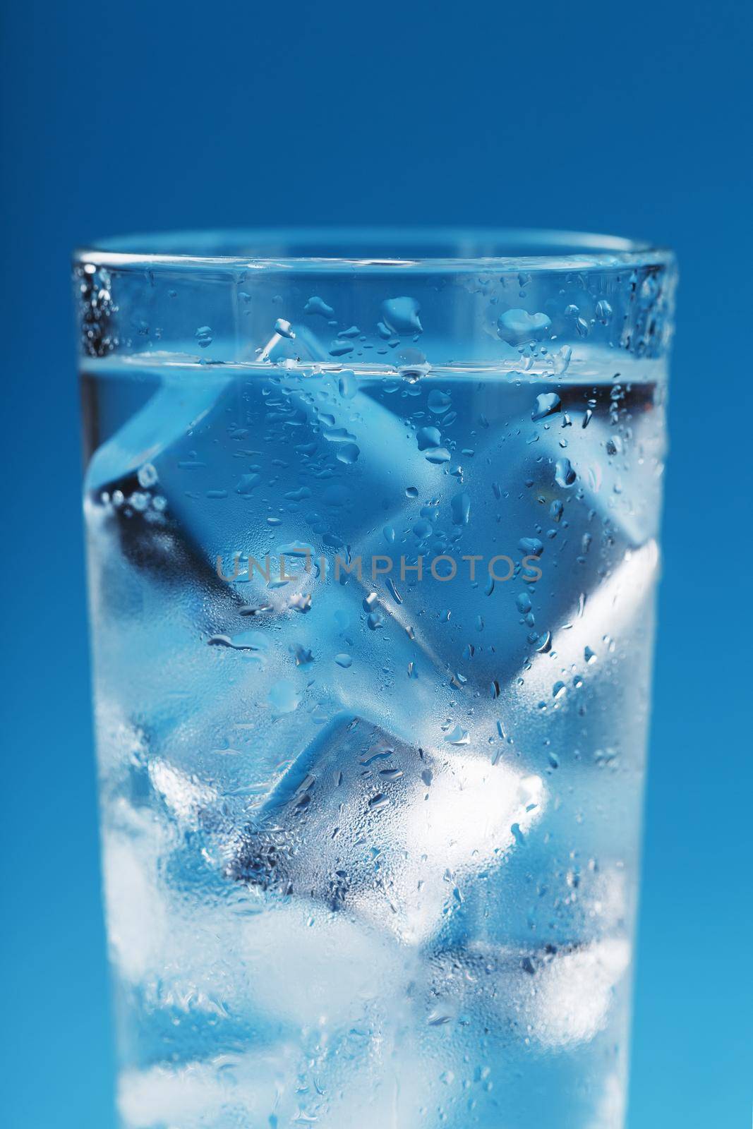 A glass with ice water and ice cubes on a blue background. A refreshing and chilling drink in hot weather.