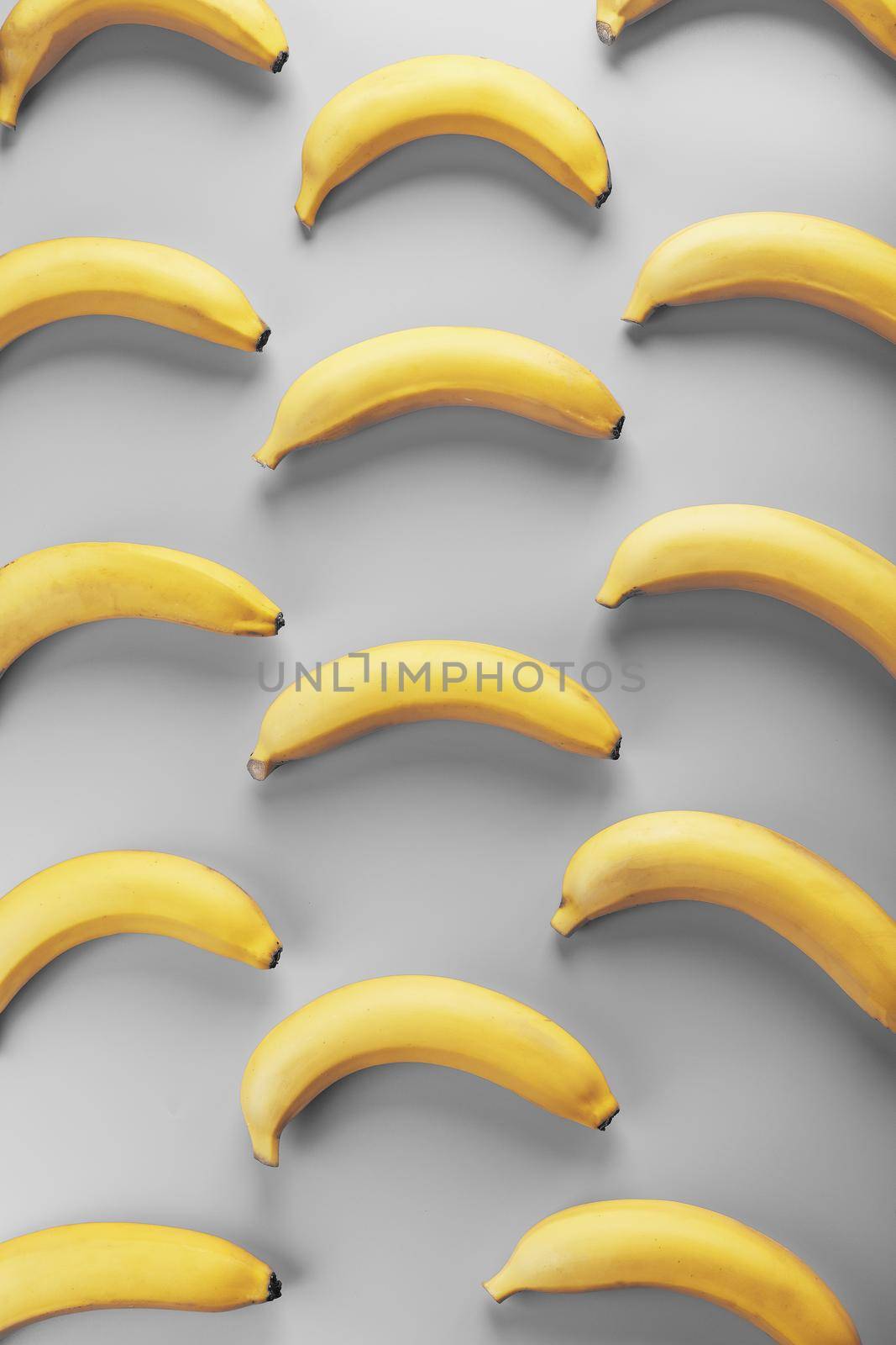 Geometric pattern of yellow bananas on a gray background in the Fashionable colors of 2021. Top view. Minimal flat style. Pop art design, creative summer concept.