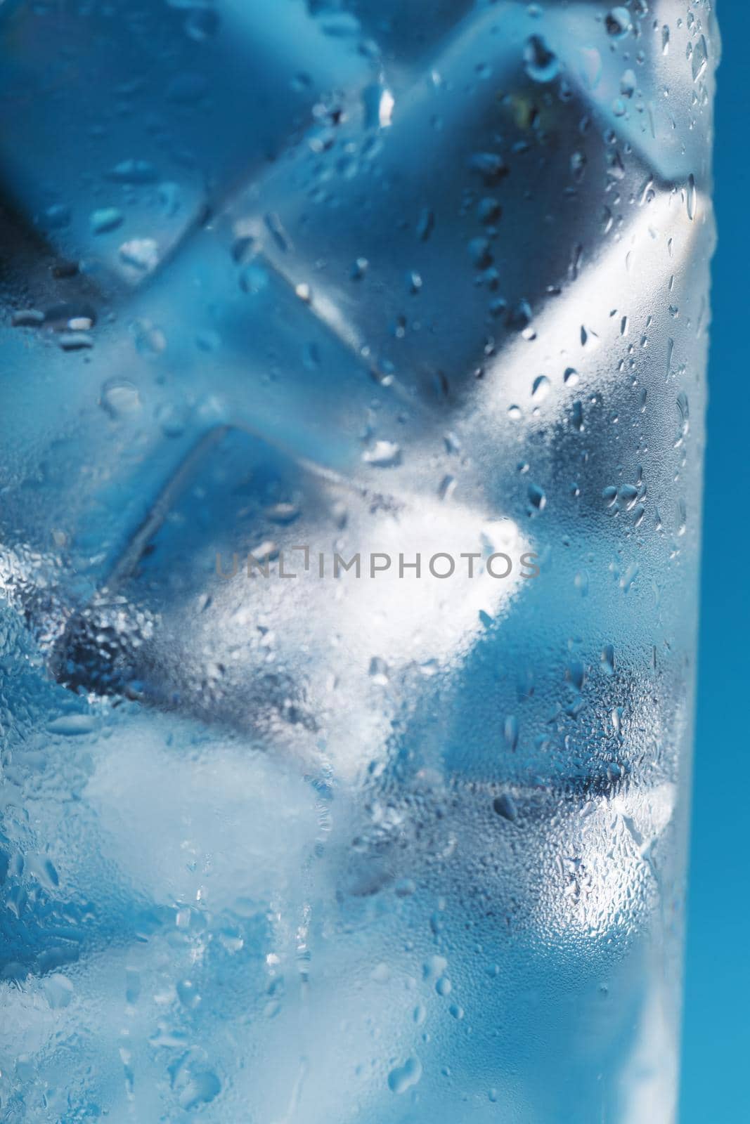 Ice cubes in a misted glass with drops of ice water close-up macro. Refreshing and chilling drink in hot weather. Blue background. Soft Selective Focus