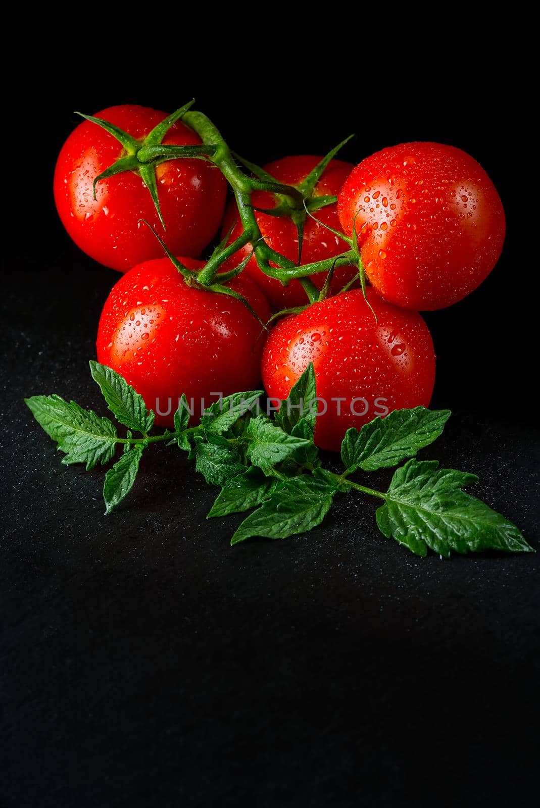 Organic tomatoes on the black table in low key, with water drops