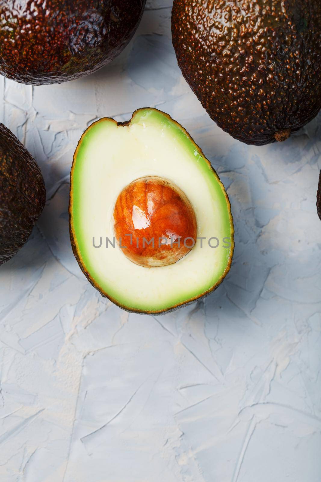 Avocado halves with whole Hass fruits on a background of gray concrete, stone or slate. Top view with copy space.