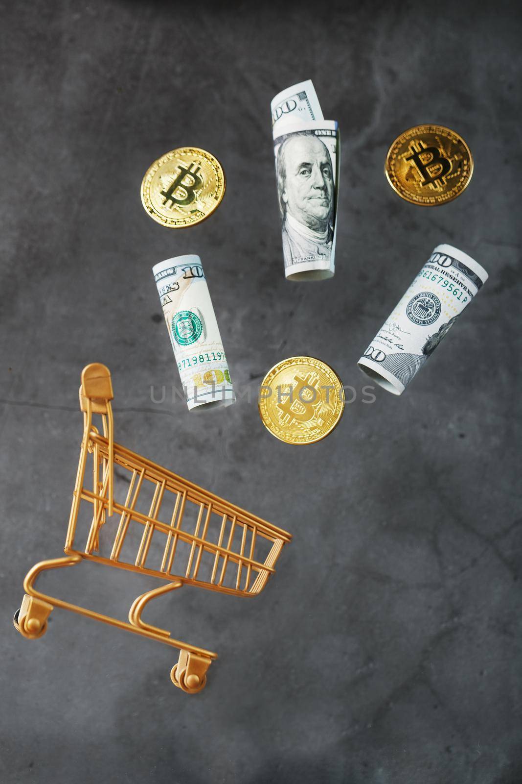 Gold mini cart with bitcoin coins and US dollars in a flight of levitation on a dark background. A shopping concept for cryptocurrency businesses, finance, trading, or stock exchange investments