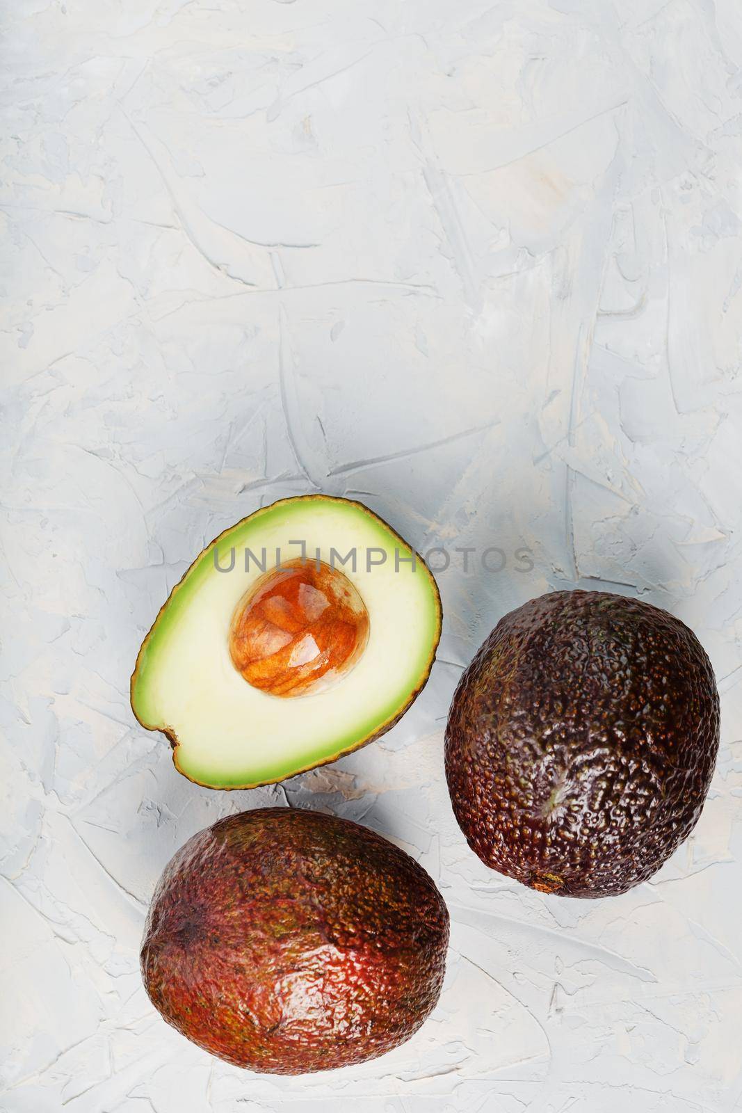 Avocado halves with whole Hass fruits on a background of gray concrete, stone or slate. by AlexGrec