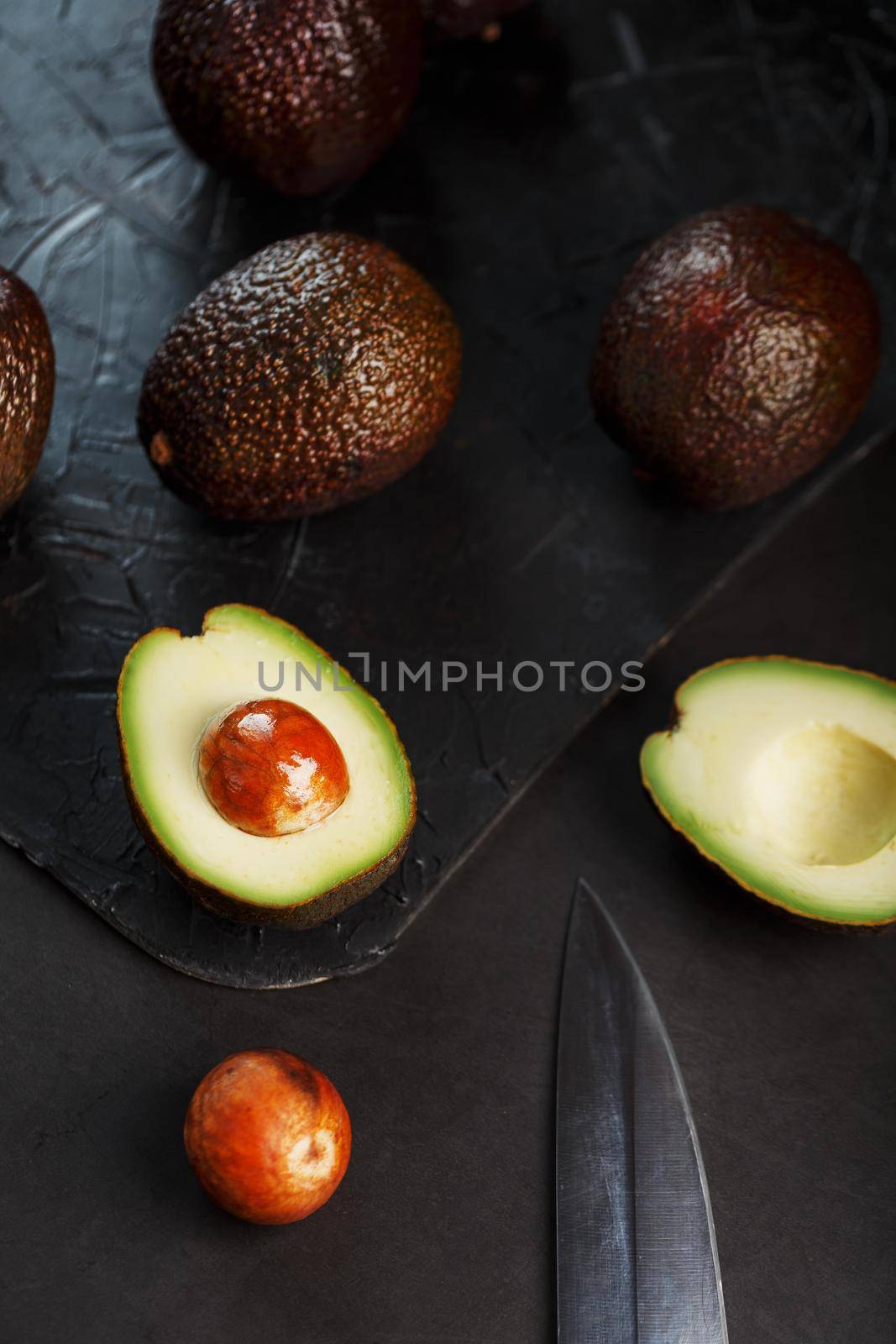 Ripe avocados in a basket on a black table, with a cut fruit and a stone. by AlexGrec