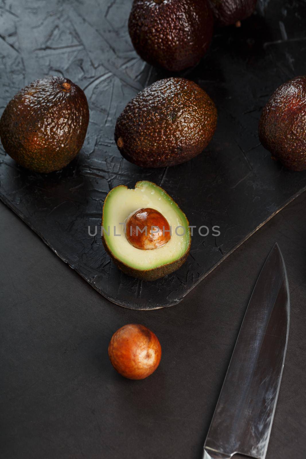 Ripe avocados in a basket on a black table, with a cut fruit and a stone. Free space, top view