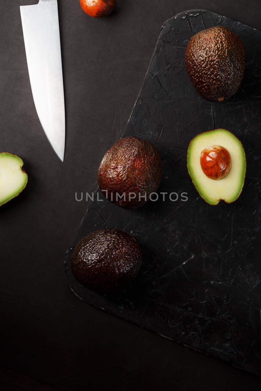 Ripe avocados in a basket on a black table, with a cut fruit and a stone. by AlexGrec
