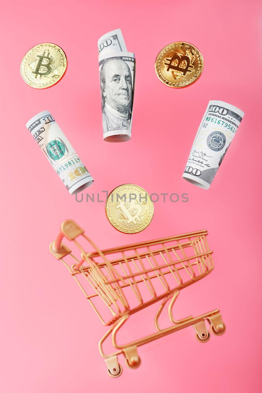Gold mini cart with bitcoin coins and US dollars in a flight of levitation on a pink background. A shopping concept for cryptocurrency businesses, finance, trading, or stock exchange investments