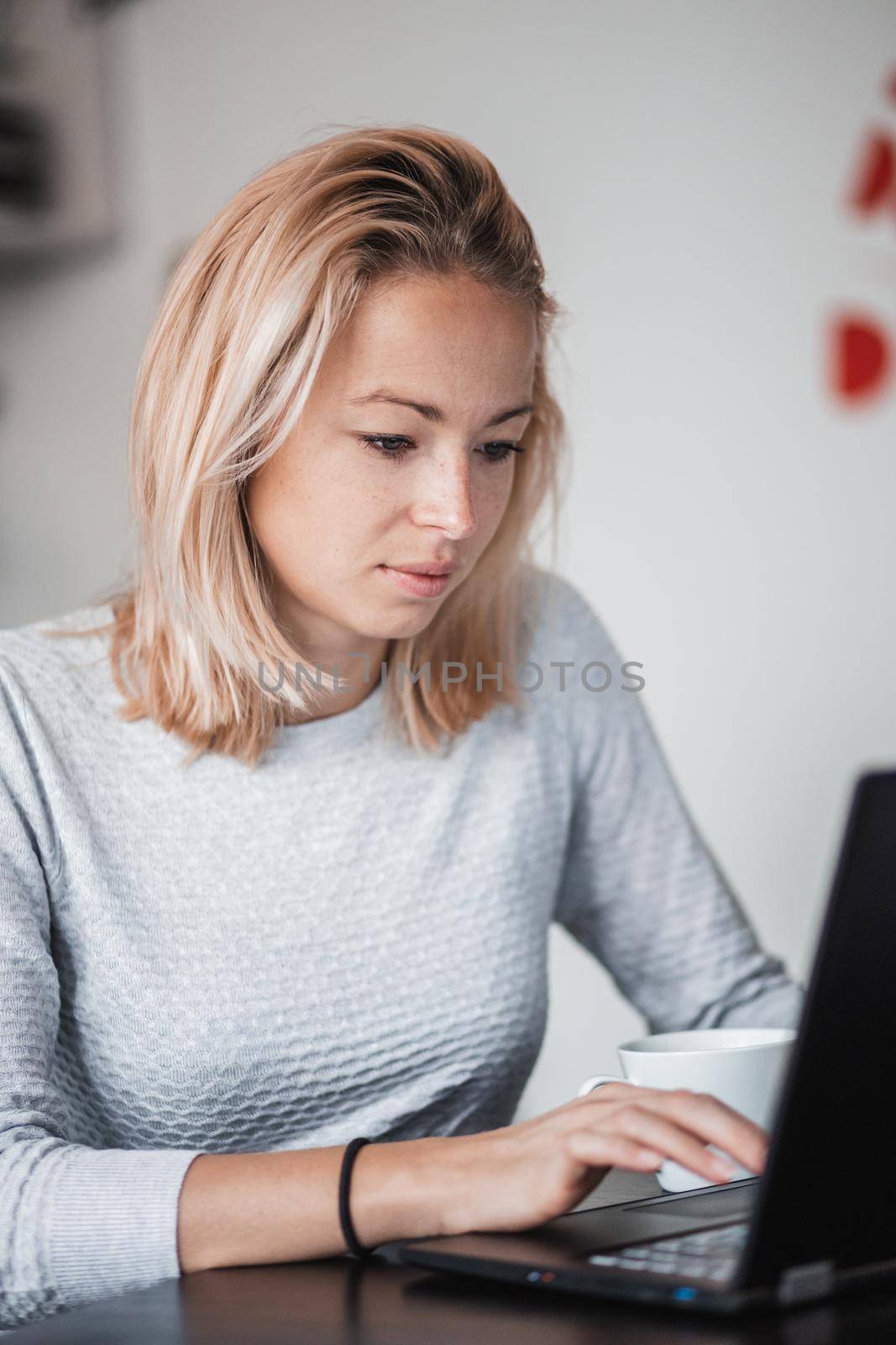 Female freelancer in her casual home clothing working remotly from her dining table in the morning. Home kitchen in the background