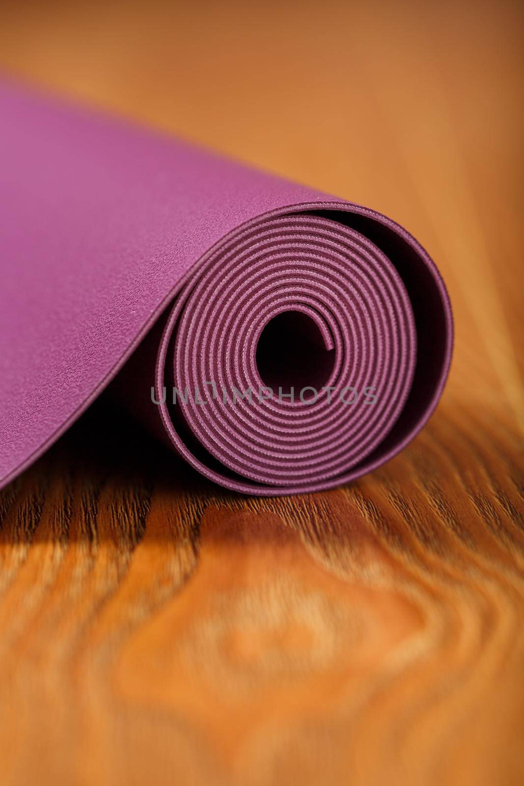 A lilac-colored yoga mat is spread out in a roll on the wooden floor. by AlexGrec