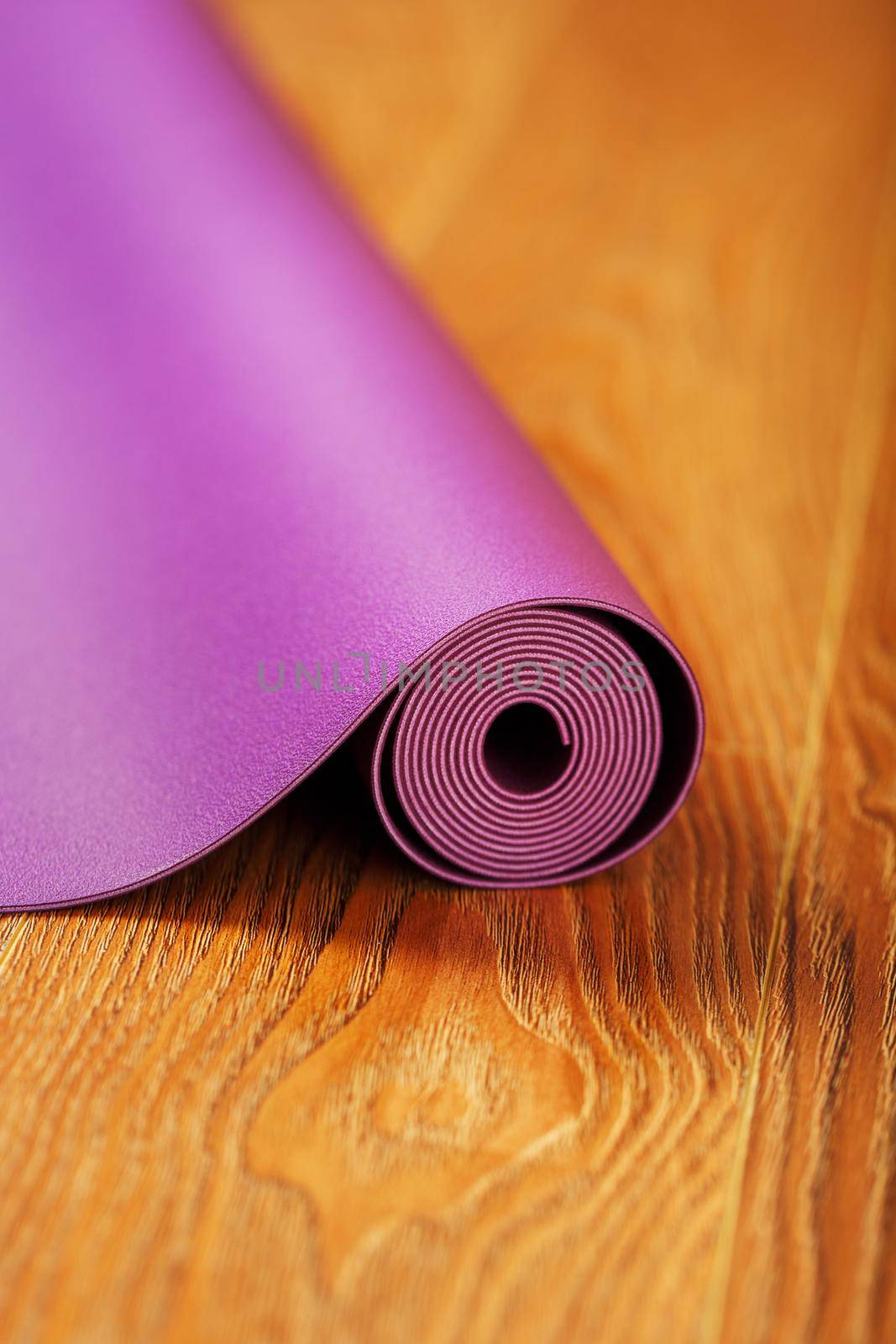 Purple yoga and fitness mat on wooden floor.