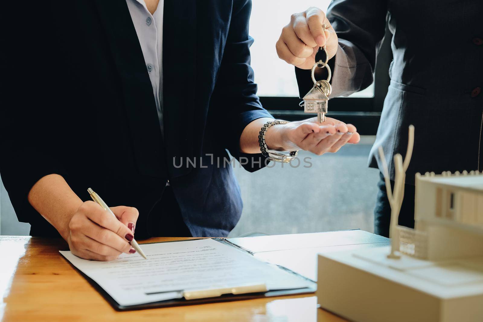 estate agent giving house keys to woman and sign agreement in office by nateemee