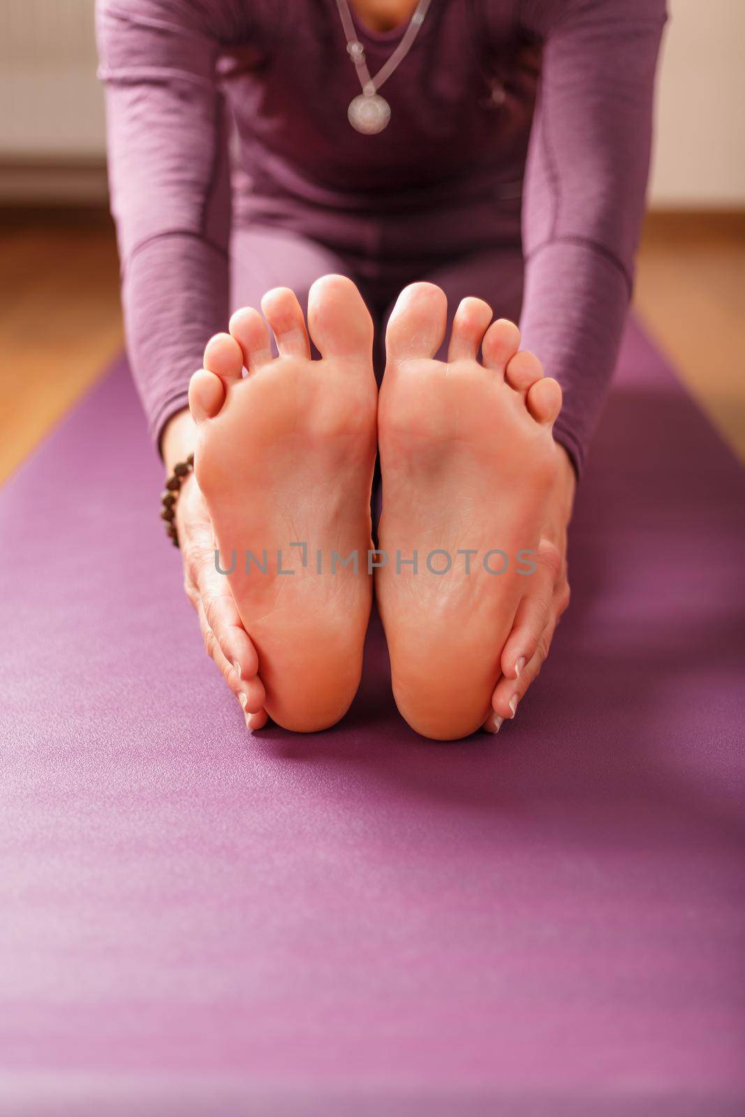 Legs and hands of a woman on a yoga mat practicing asanas by AlexGrec