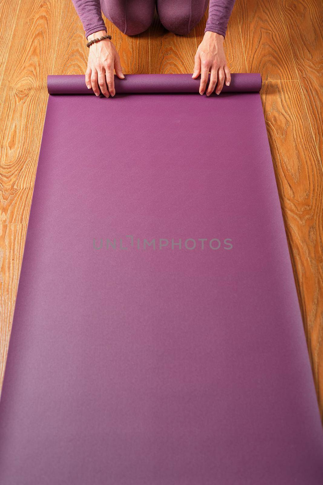 A woman's hands fold a lilac yoga or fitness mat after a workout at home in the living room. Healthy lifestyle, asana and meditation practices
