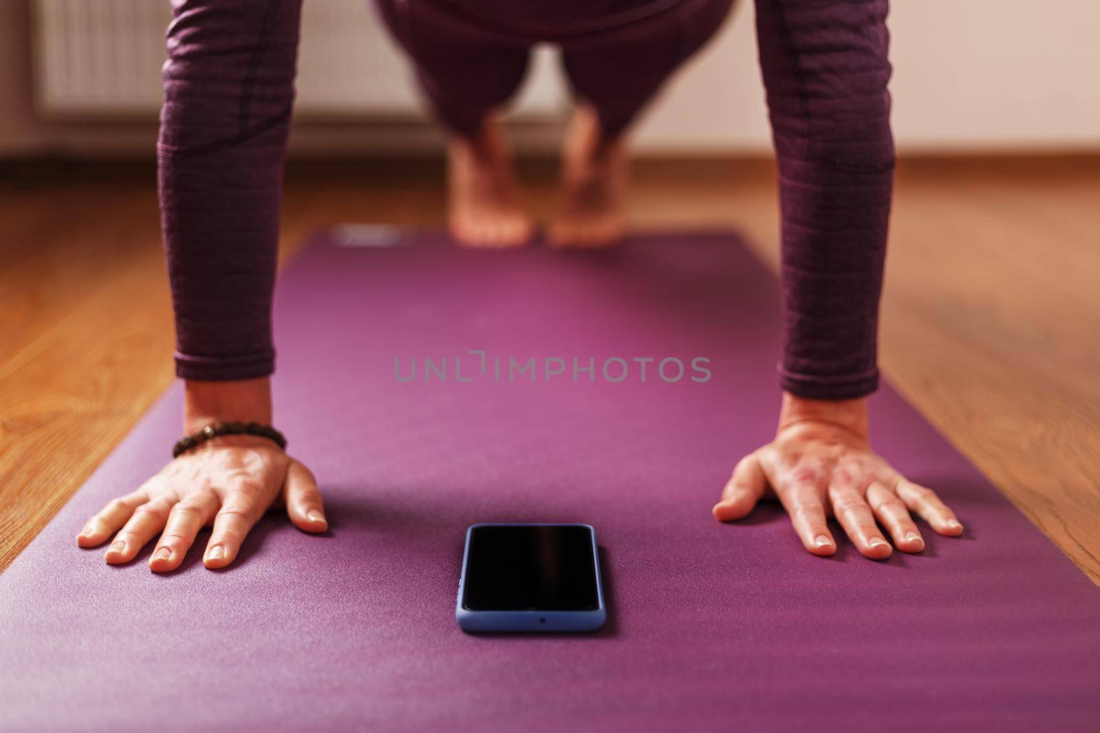 A girl does yoga with a smartphone in the asana stand on a lilac mat. Trainer, online training, online video yoga instructor, modern smartphone screen, meditation.