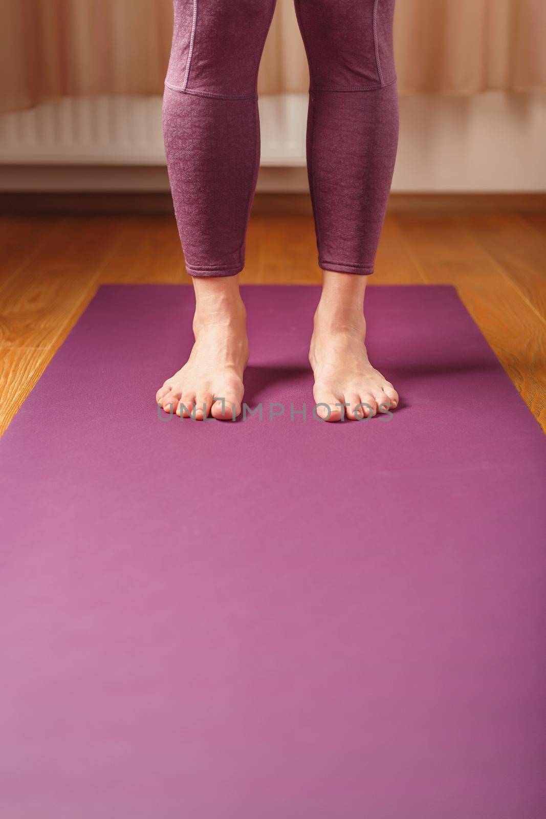 Legs and hands of a woman on a yoga mat practicing asanas by AlexGrec