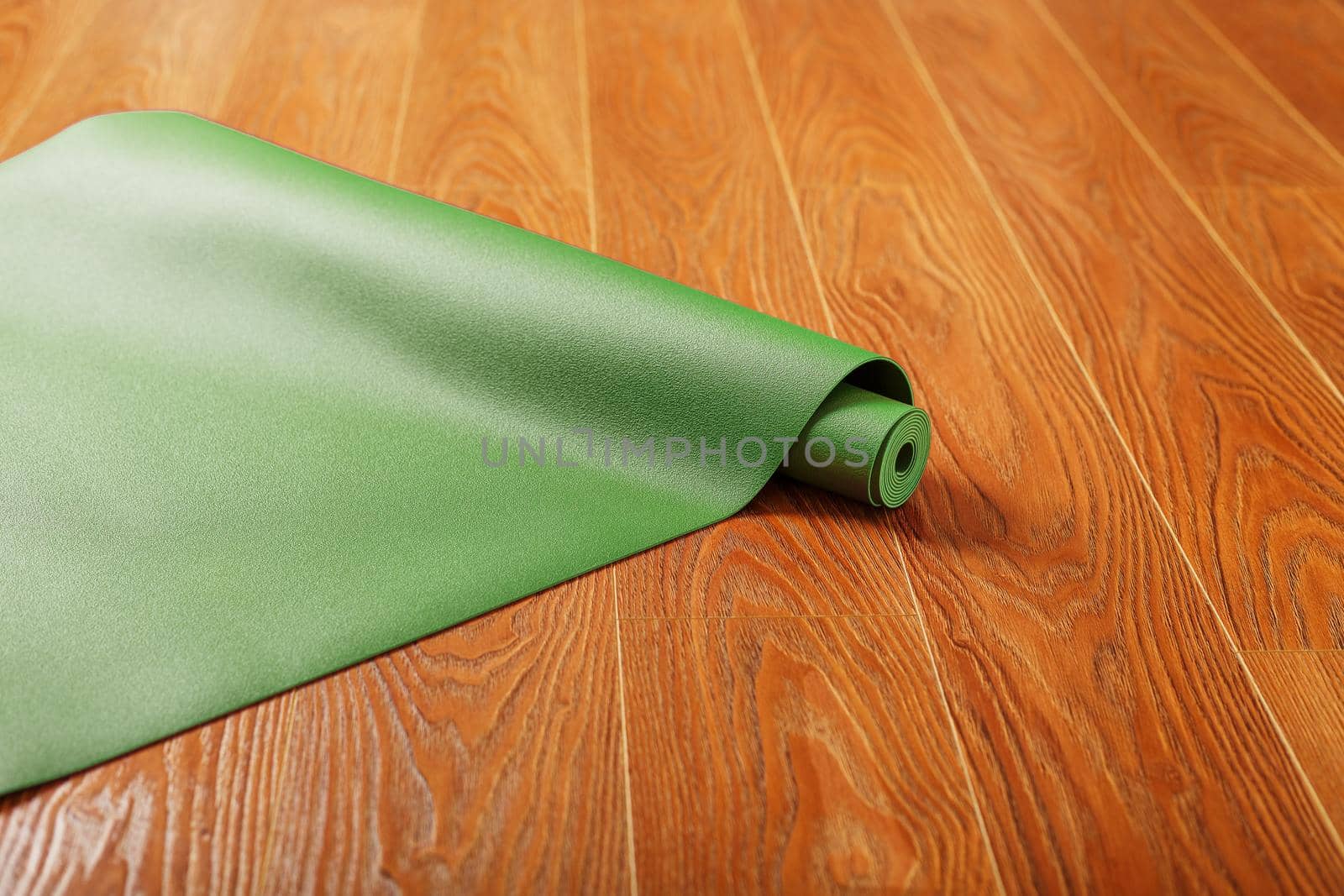A green yoga mat is laid out in a roll on the wooden floor. A healthy lifestyle in isolation.