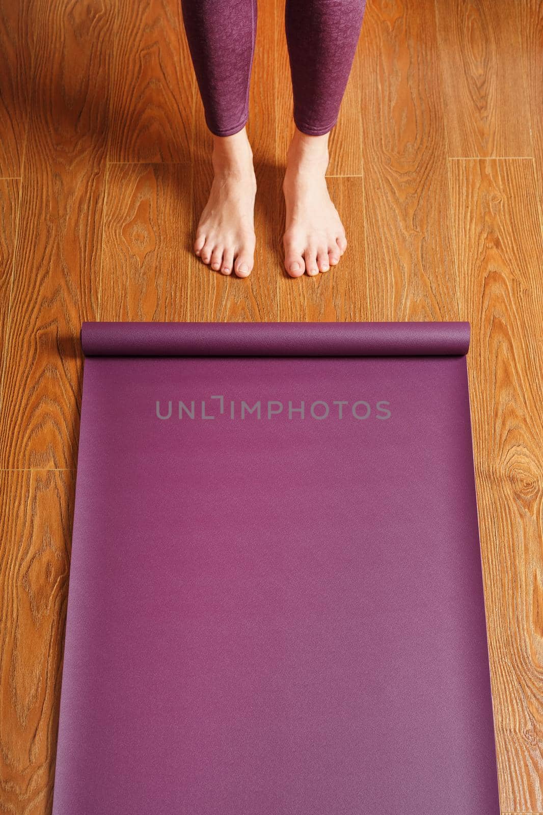 A woman lays out a lilac yoga mat on the wooden floor. Women practicing yoga. A healthy lifestyle in isolation.