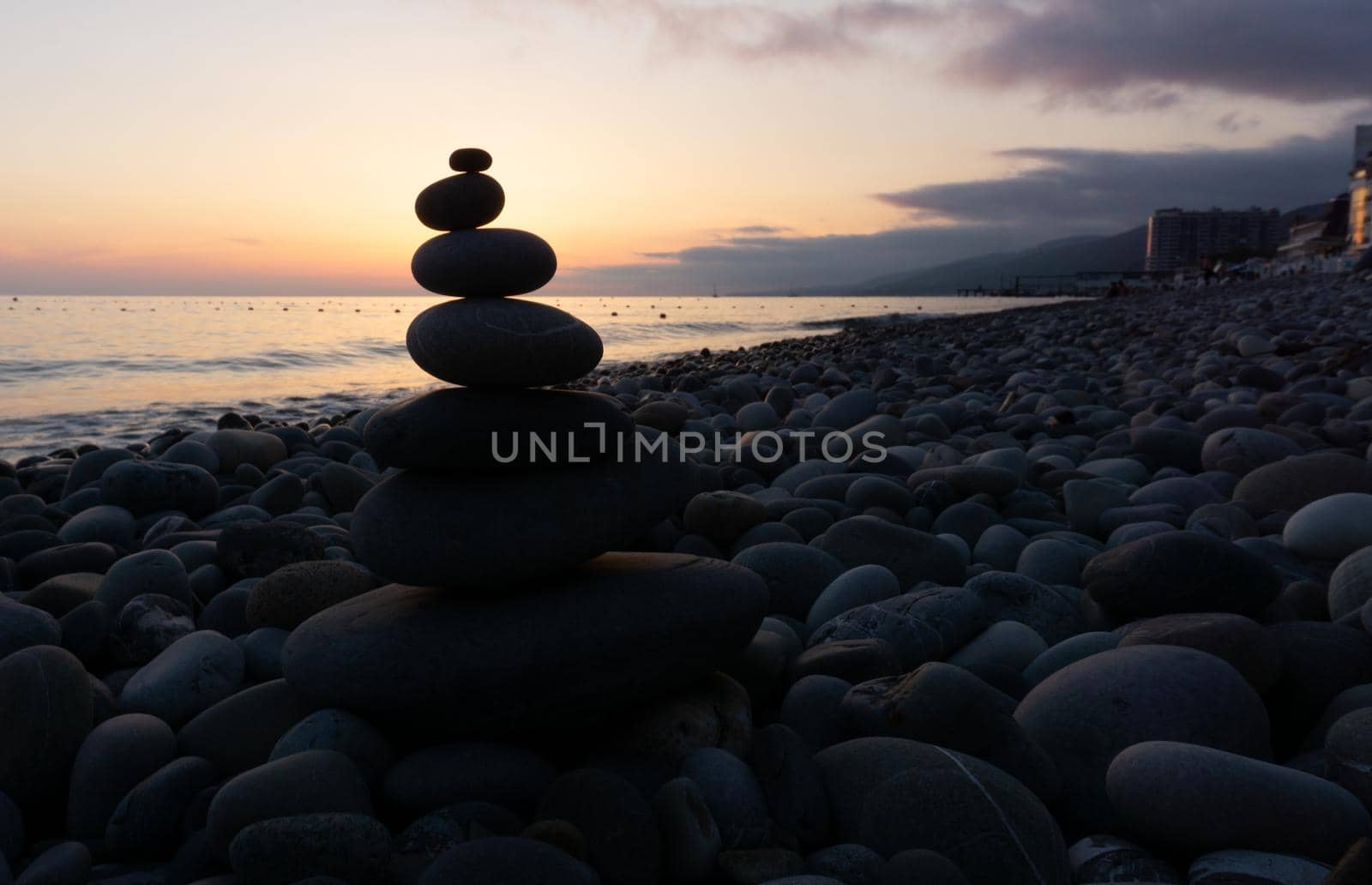 Stack of gray zen stones on the beach at sunset, beautiful seascape. Made of stone tower as rest balance vacation concept.