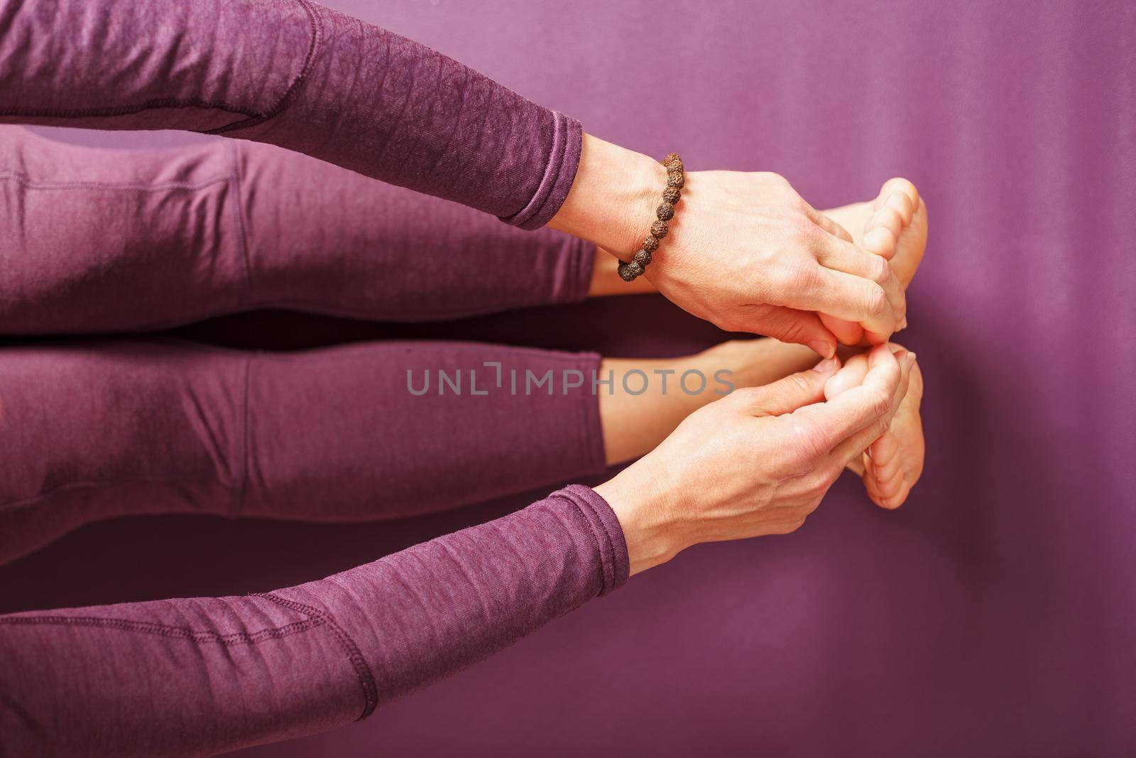 Legs and hands of a woman on a yoga mat practicing asanas by AlexGrec