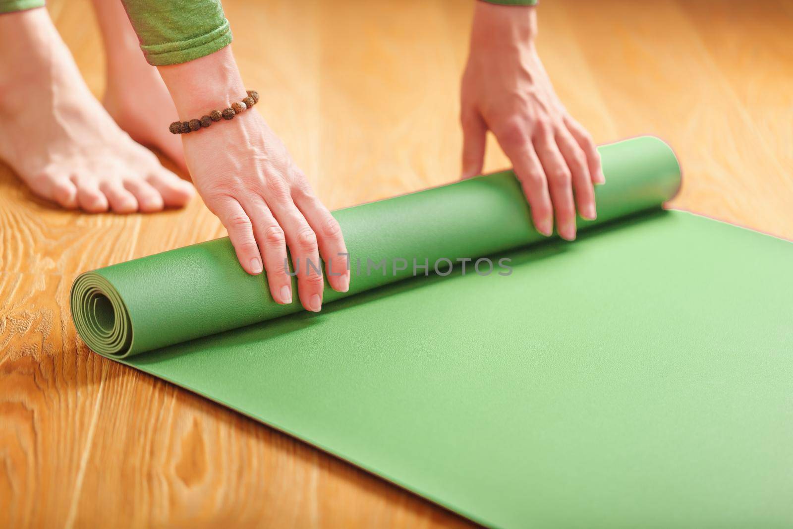 A woman rolls out a green mat before a yoga class by AlexGrec