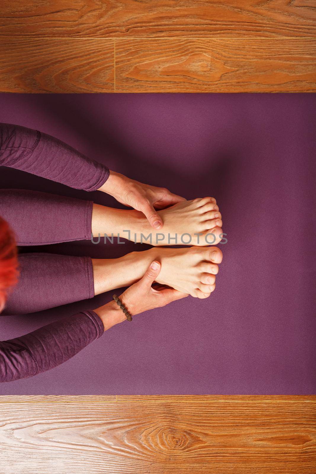 Girl practicing yoga leaning forward sitting, feet forward-paschimottanasana pose, training on a lilac mat.