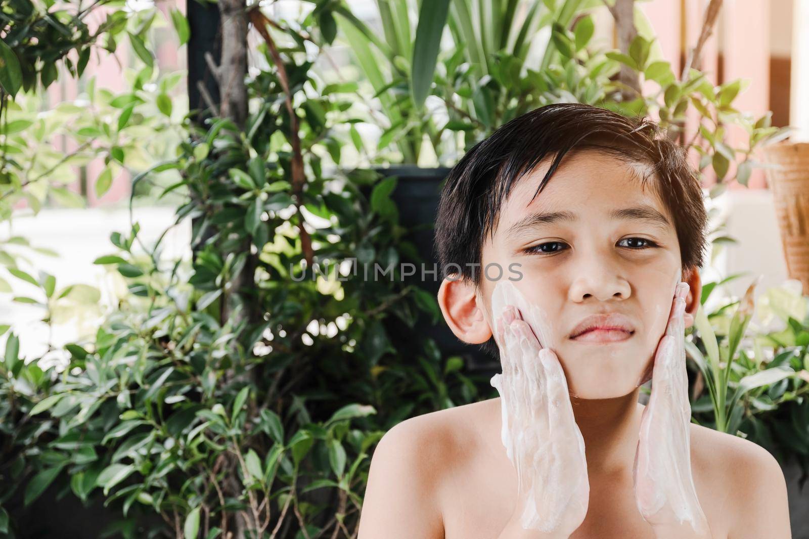 Asian boy is cleaning his face with a foaming cleanser. by wattanaphob