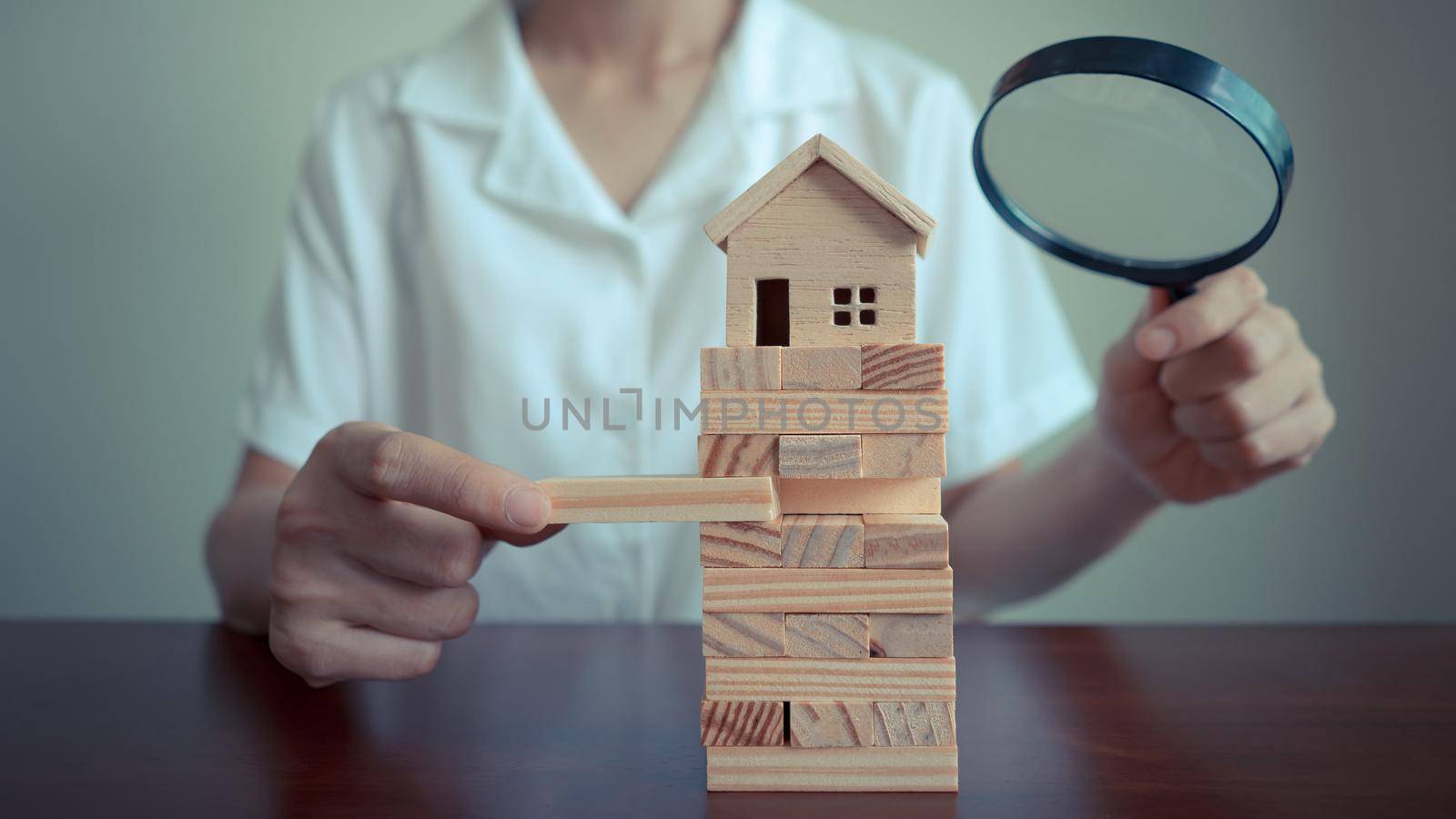 Female complete wooden model of the house with last piece and using magnifying glass over the model of a wooden house. Concept of House Search and Insurance.