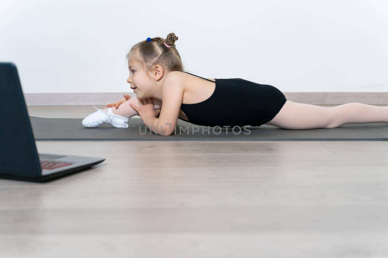 kid girl in a gymnastic leotard practices yoga with a trainer online. A child plays sports during the COVID-19