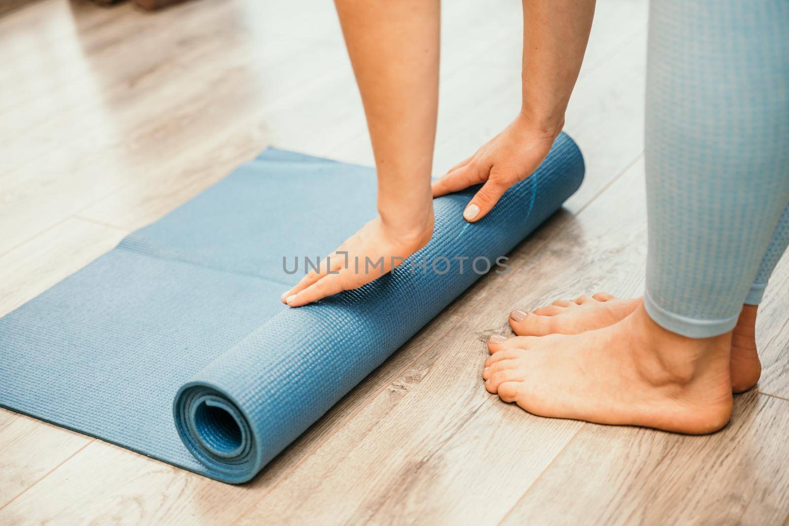 Woman hands rolled up yoga mat on gym floor in yoga fitness training room. Home workout woman close up hands rolling foam yoga gym mat. Woman barefoot home workout sportive healthy lifestyle concept by Matiunina