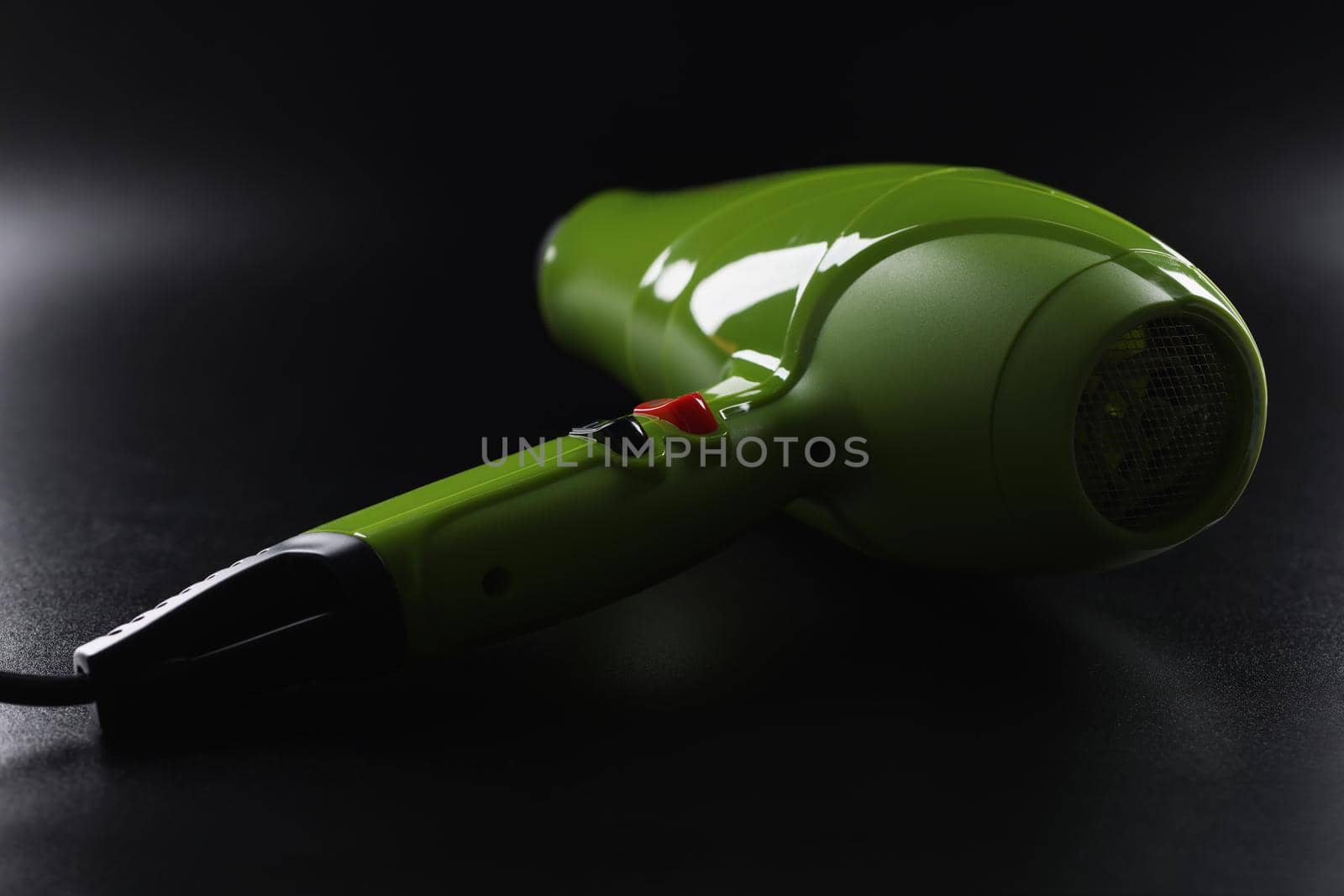 Close-up of green professional hairdryer device lay on black background, tool for beauty master. Equipment make hot air and dry hair. Beauty salon concept