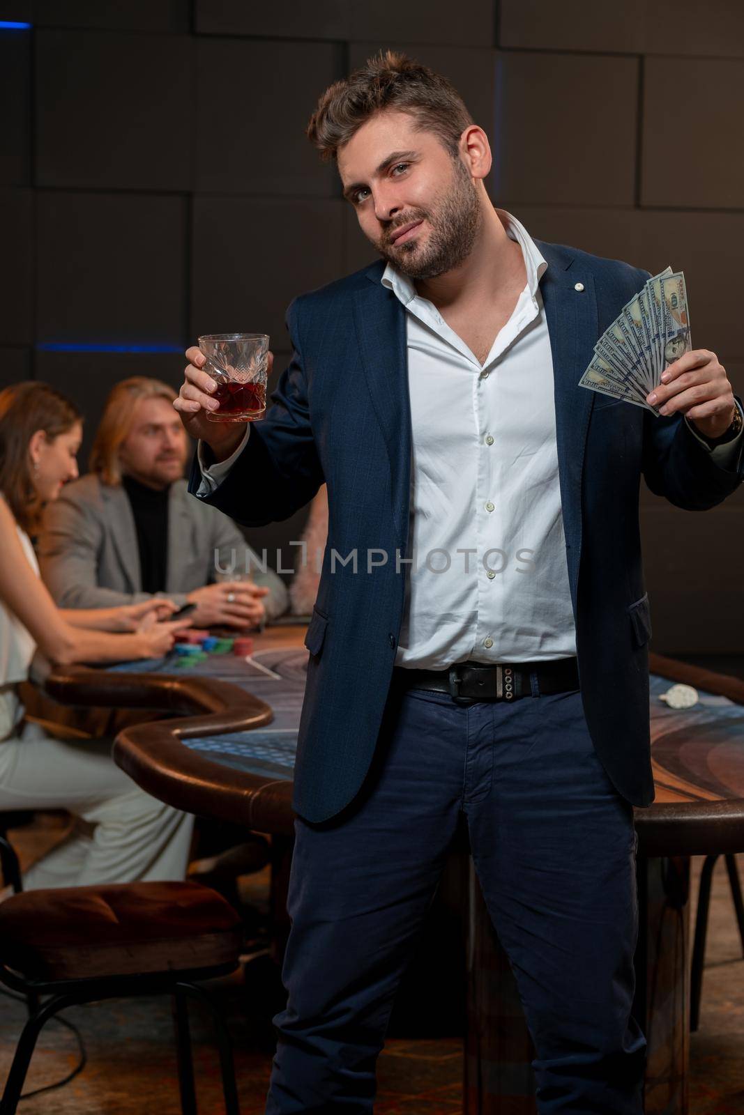 Successful guy standing with banknotes and glass of alcohol near poker table by nazarovsergey