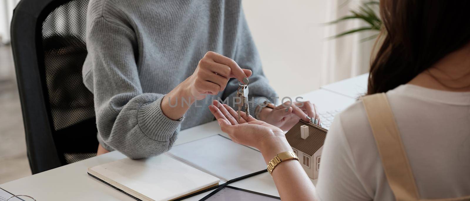 real estate agent holding house key to his client after signing contract agreement in office,concept for real estate, moving home or renting property.