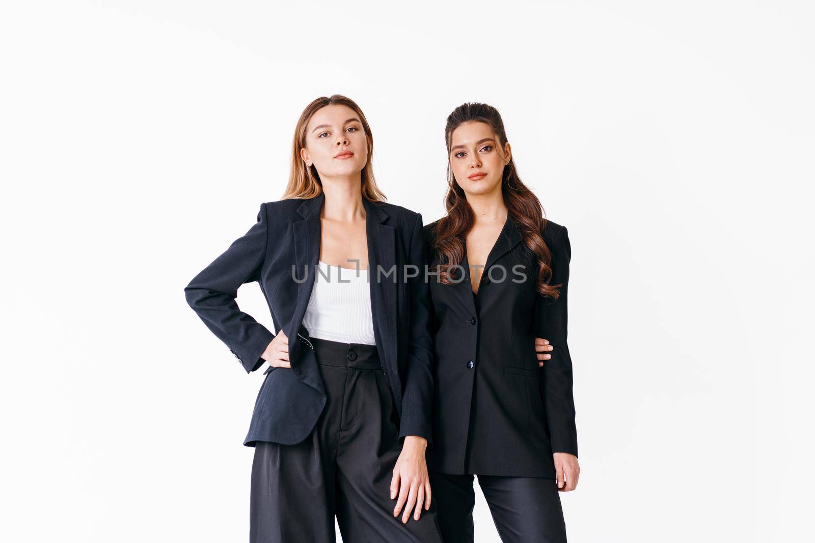 Concept of partnership in business. Two Young businesswoman dressed black formal suit standing studio isolated white background. Blonde and brunette woman friends, Fashion, Caucasian female
