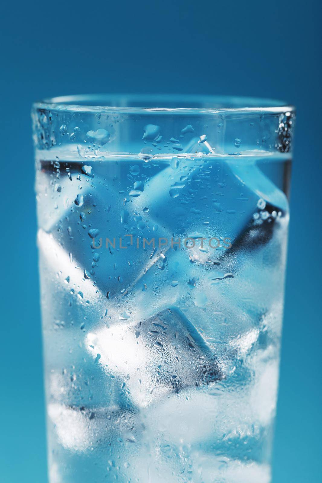 Ice cubes in a glass with refreshing ice water on a blue background. Close-up